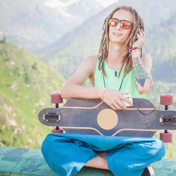 Hippie gutaussehender Mann mit Skateboard und Handy beim Musikhören — Stockfoto