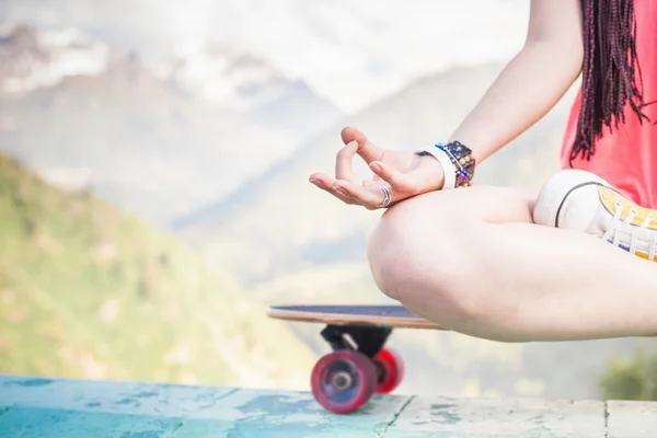 Хиппи мода девушка делает йогу, расслабляясь на скейтборде в горах — стоковое фото