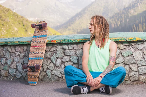 Ritratto di uomo bello fresco e divertente con skateboard in montagna — Foto Stock