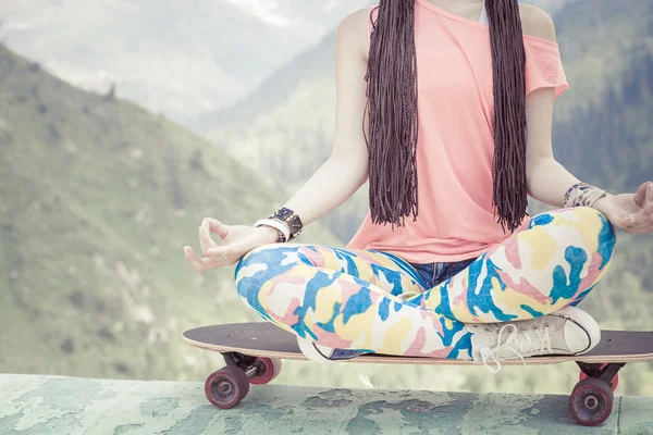 Hipster fashion girl doing yoga, relaxing on skateboard at mountain — Stock Photo, Image