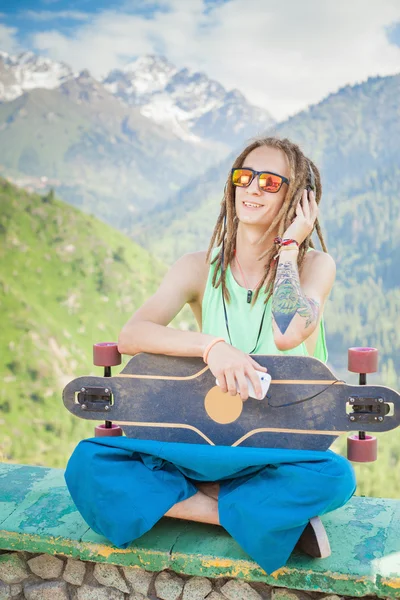 Hipster gutaussehender Mann mit Skateboard und Handy beim Musikhören — Stockfoto