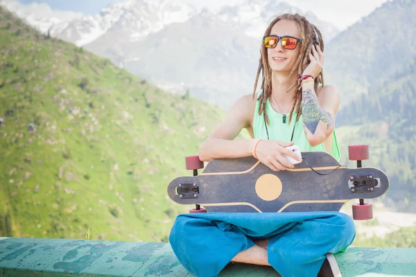 Hipster gutaussehender Mann mit Skateboard und Handy beim Musikhören — Stockfoto