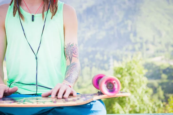 Entspannter und gutaussehender Hipster, der mit Skateboard Musik hört — Stockfoto