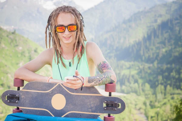 Hipster gutaussehender Mann mit Skateboard und Handy beim Musikhören — Stockfoto