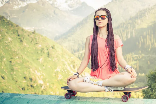 Hipster ragazza di moda che fa yoga, relax su skateboard in montagna — Foto Stock
