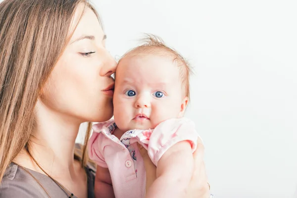 Mãe feliz beijando seu bebê no fundo branco — Fotografia de Stock