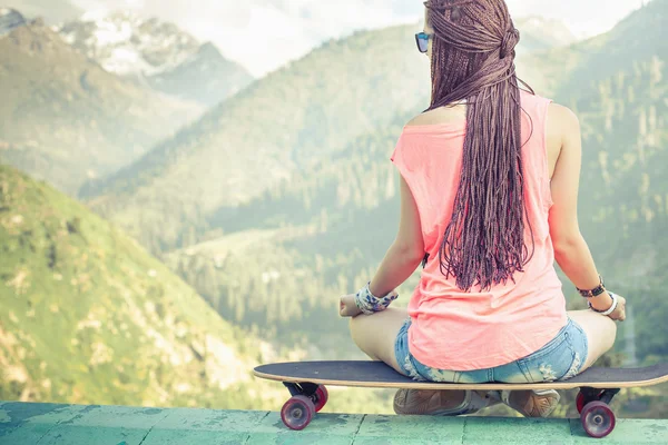 Hipster chica de la moda haciendo yoga, relajarse en el monopatín en la montaña — Foto de Stock