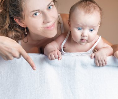 Mother with baby lying on white blanket and pointing down