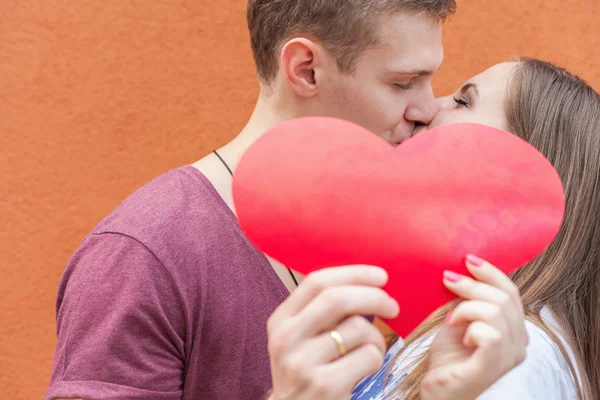 Happy couple kissing and holding a heart at red background — Stok fotoğraf