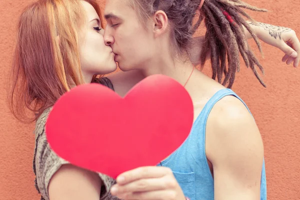 Feliz pareja besándose y sosteniendo el corazón en el fondo rojo de la pared — Foto de Stock