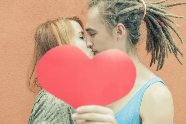 Feliz pareja besándose y sosteniendo el corazón en el fondo rojo de la pared — Foto de Stock