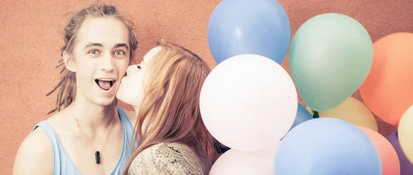 Young happy couple near the orange wall stand with balloons — Stok fotoğraf