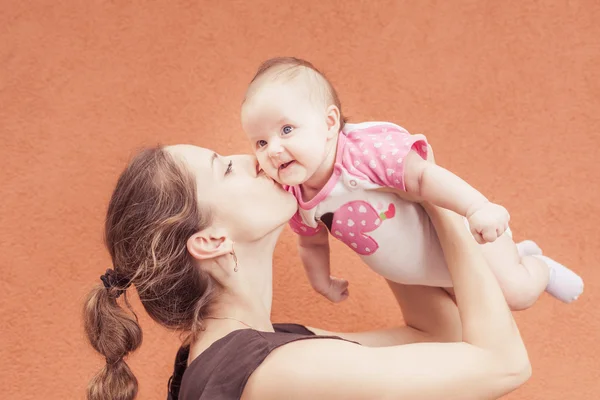 Счастливая мать целует своего ребенка на фоне стены — стоковое фото