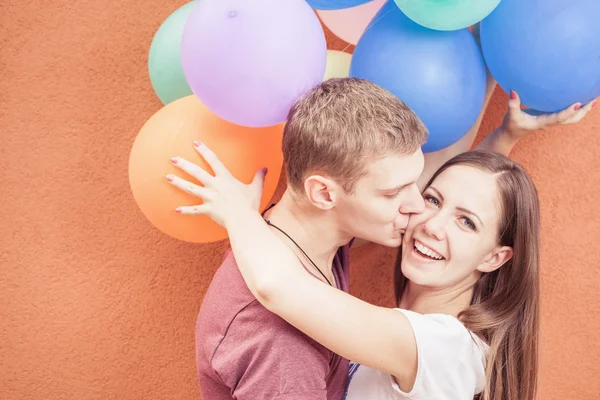 Молодая счастливая пара возле оранжевой стены стенда с воздушными шарами — стоковое фото