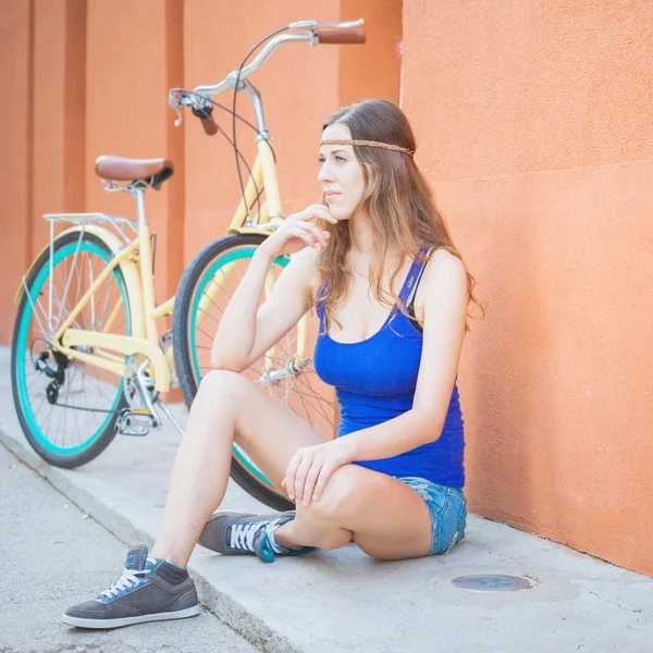 Fashion beautiful woman sitting near the wall and vintage bicycle — Stock Photo, Image