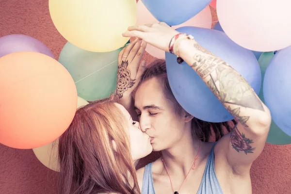 Glückliches und lustiges Paar küsst sich im Hintergrund der bunten Luftballons — Stockfoto