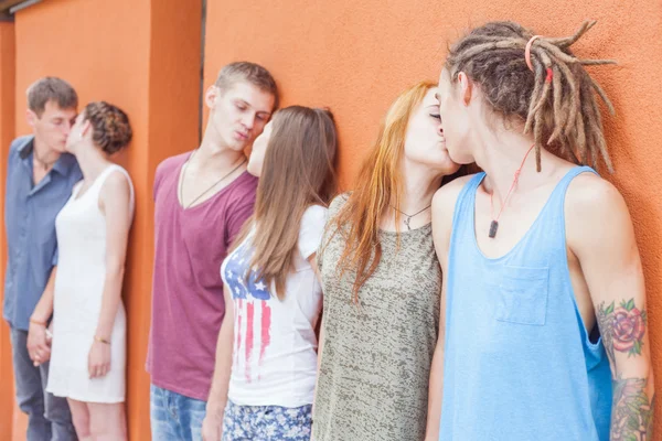 Medium group of people kissing and standing near red wall background — стоковое фото