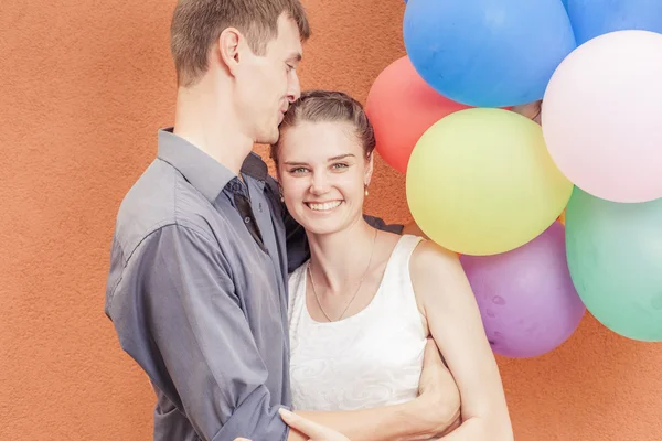 Joven pareja feliz cerca del soporte de pared naranja con globos —  Fotos de Stock