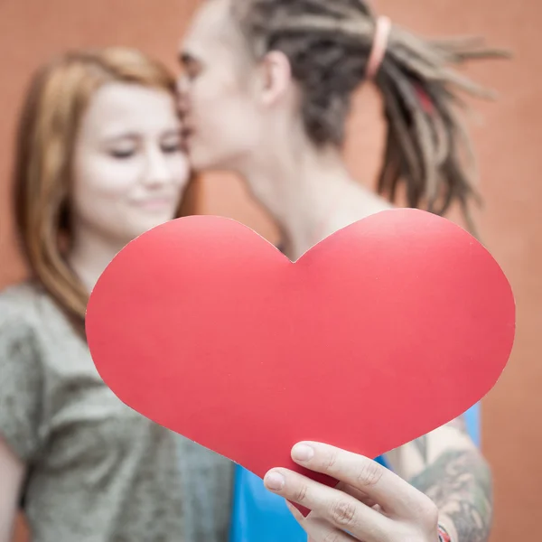 Happy couple kissing and holding heart at red wall background — 图库照片