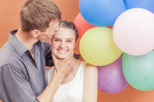 Joven pareja divertida cerca del soporte de pared naranja con globos —  Fotos de Stock