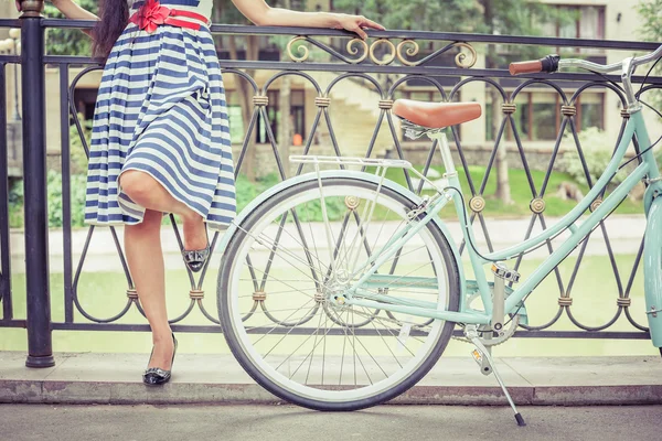 Chica joven de pie cerca de la cerca cerca de la bicicleta vintage en el parque — Foto de Stock