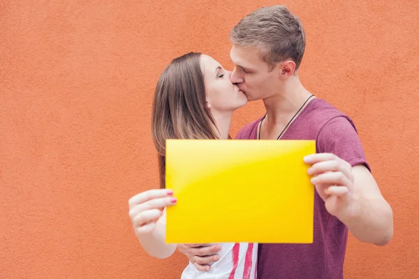 Young couple kissing and holding frame at background of wall — Stok fotoğraf