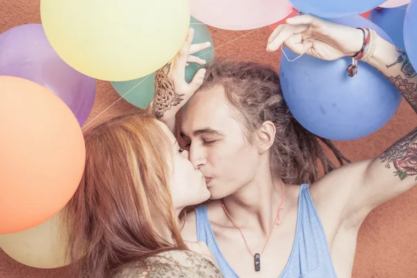 Feliz y divertida pareja besándose en el fondo de globos de color — Foto de Stock