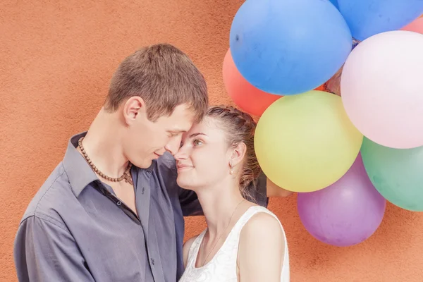 Joven pareja feliz cerca del soporte de pared naranja con globos —  Fotos de Stock