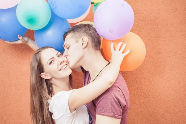 Young happy couple kissing near orange wall stand with balloons — Zdjęcie stockowe