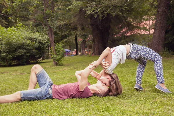 Joven pareja besos inusuales al aire libre en el parque, en posición extrema — Foto de Stock