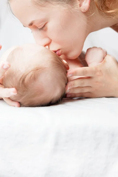 Glad mamma kysser en baby, liggande på en vit säng — Stockfoto