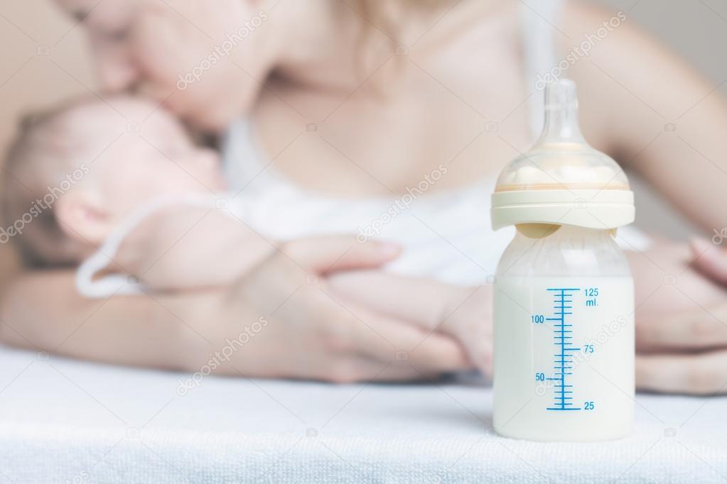 Baby bottle with breast milk and mother with baby