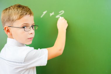 First grade schoolboy wrote on blackboard with chalk at classroom