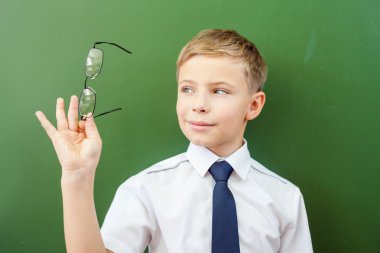 Happy schoolboy standing near the blackboard with medical glasses