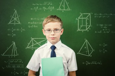 Smart student or schoolboy with a notebook standing near blackboard