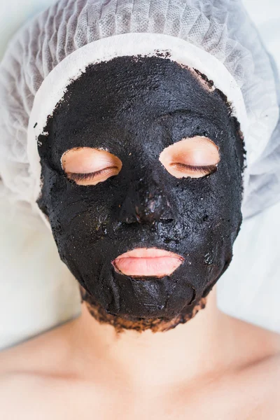 Woman in spa salon with black mud face mask — Stock Photo, Image