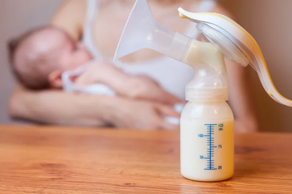 Manual breast pump with milk, mother and baby at background — Stock Photo, Image