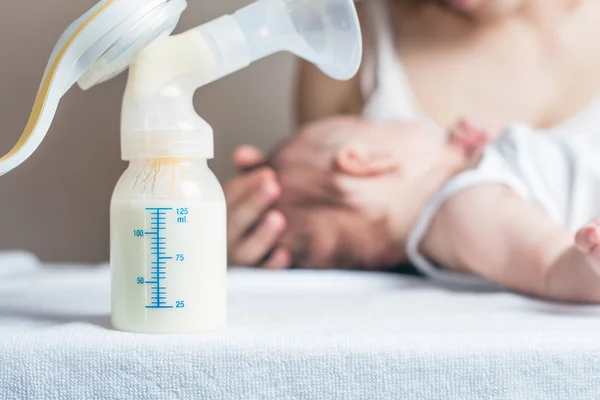 Manual breast pump with milk, mother and baby at background — Stok fotoğraf