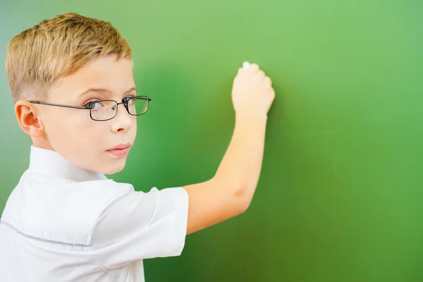 First grade schoolboy wrote on blackboard with chalk at classroom — Stock Photo, Image