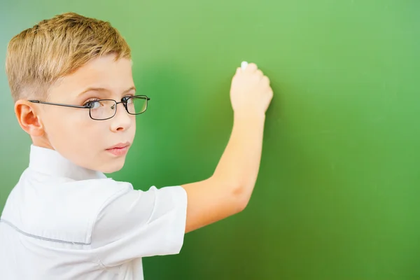 First grade schoolboy wrote on blackboard with chalk at classroom — Stock fotografie