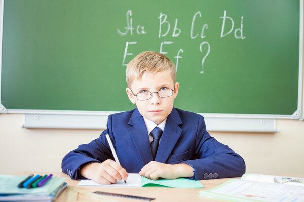 Schoolboy sits at a desk at school classroom