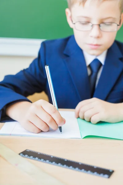 Estudante sentado na mesa na escola e escrevendo para notebook — Fotografia de Stock