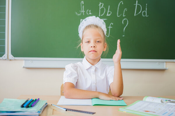 Schoolgirl sitting at desk, school classroom, on background of board