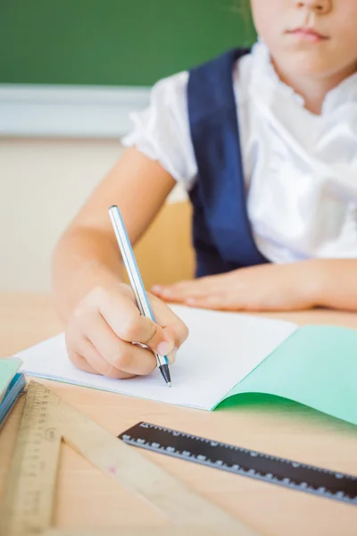 Schoolgirl sitting at desk at school and writing to notebook — Stock Photo, Image