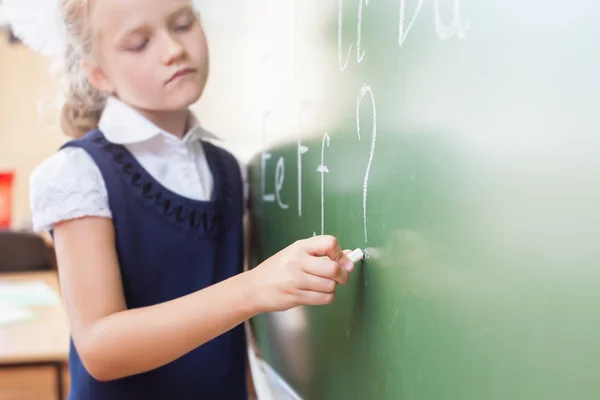 Schoolgirl writes English alphabet with chalk on blackboard — стокове фото