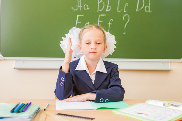 Schoolgirl sitting at desk, school classroom, on background of board