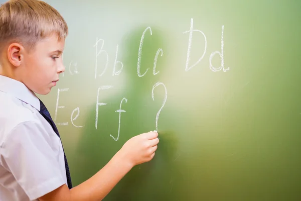 School boy scrive l'alfabeto inglese con gesso sulla lavagna — Foto Stock