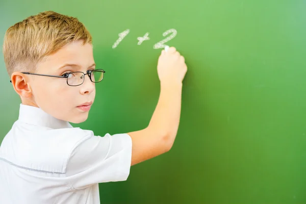 First grade schoolboy wrote on blackboard with chalk at classroom — Stock Fotó