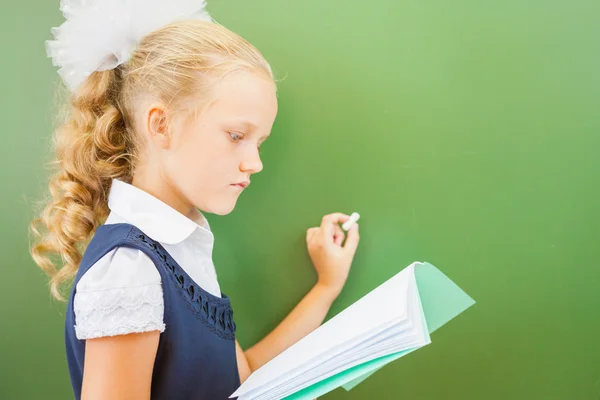 First grade schoolgirl wrote on blackboard with chalk at classroom