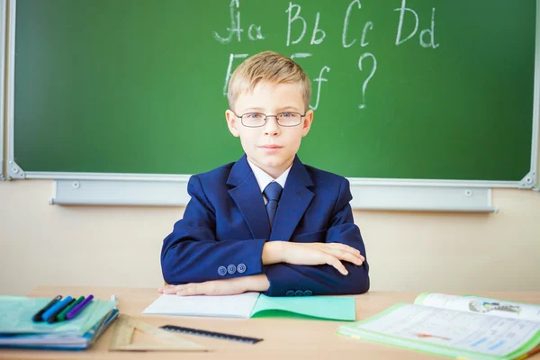 Schoolboy senta-se em uma mesa na sala de aula da escola — Fotografia de Stock
